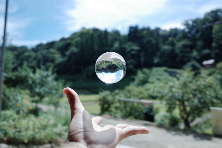 A crystal ball floats over a hand against a backdrop of greenery.
