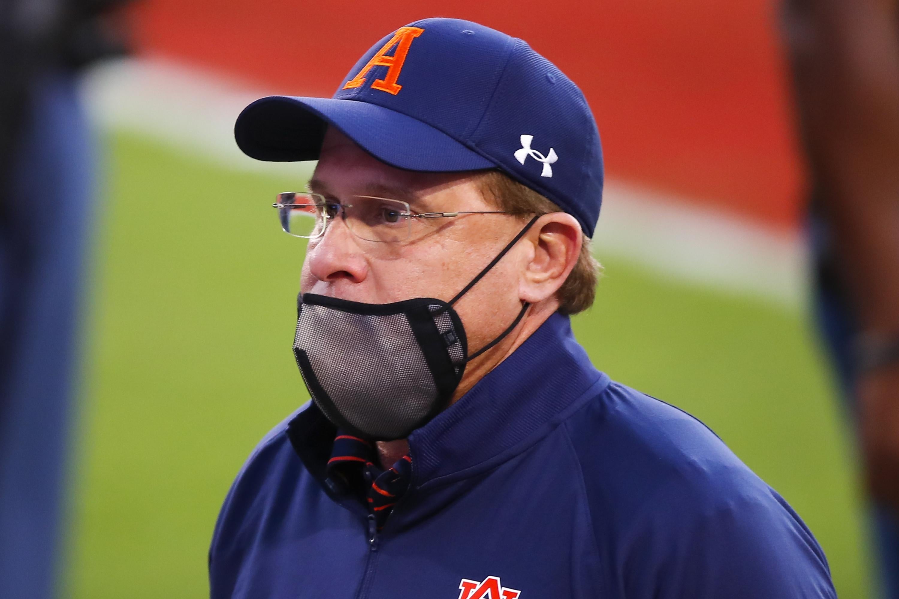Gus Malzahn in an Auburn hat with a mask pulled under his nose, on his chin