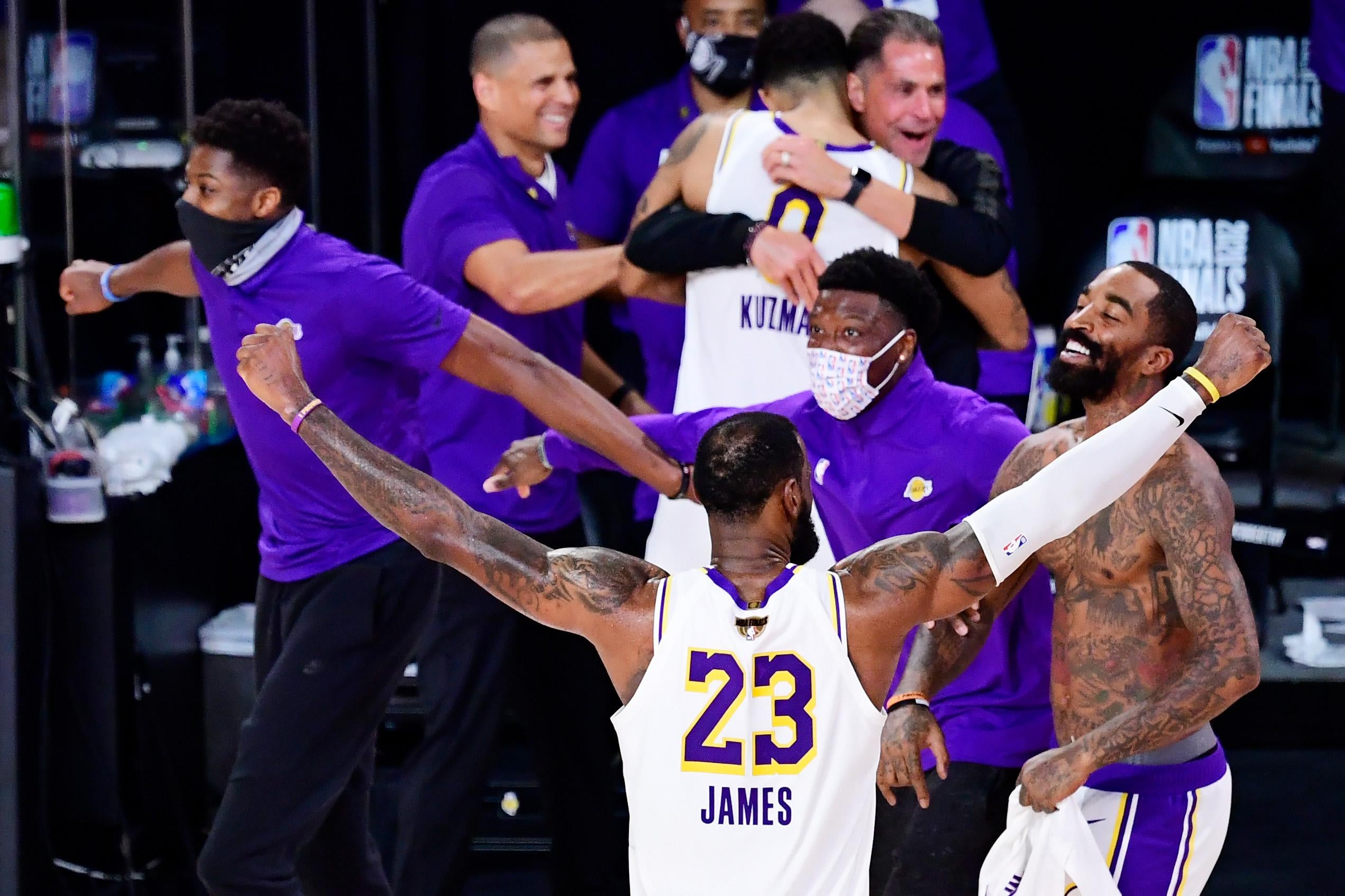 LeBron James celebrates winning the 2020 NBA Finals with his arms raised, beside smiling, shirtless teammate J.R. Smith and other Lakers in the background.