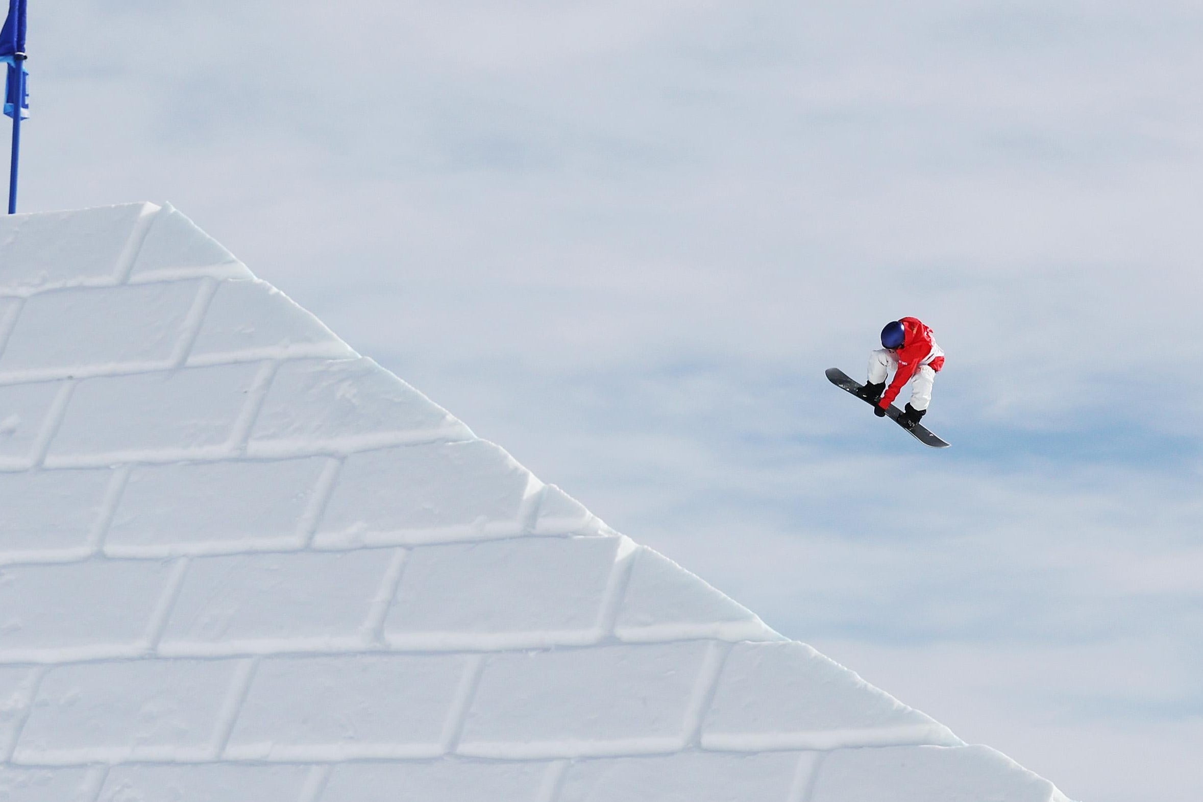 The snowboarder flies and tucks through the air over a white brick sloping wall