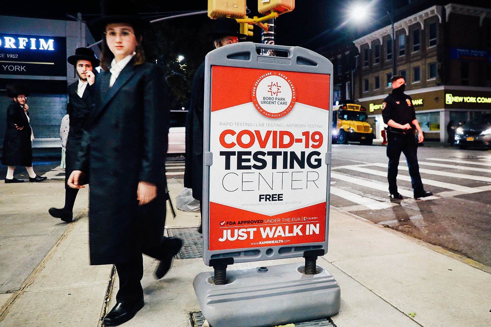 A boy in traditional Hasidic dress walks by a sign that says COVID-19 Testing Center.