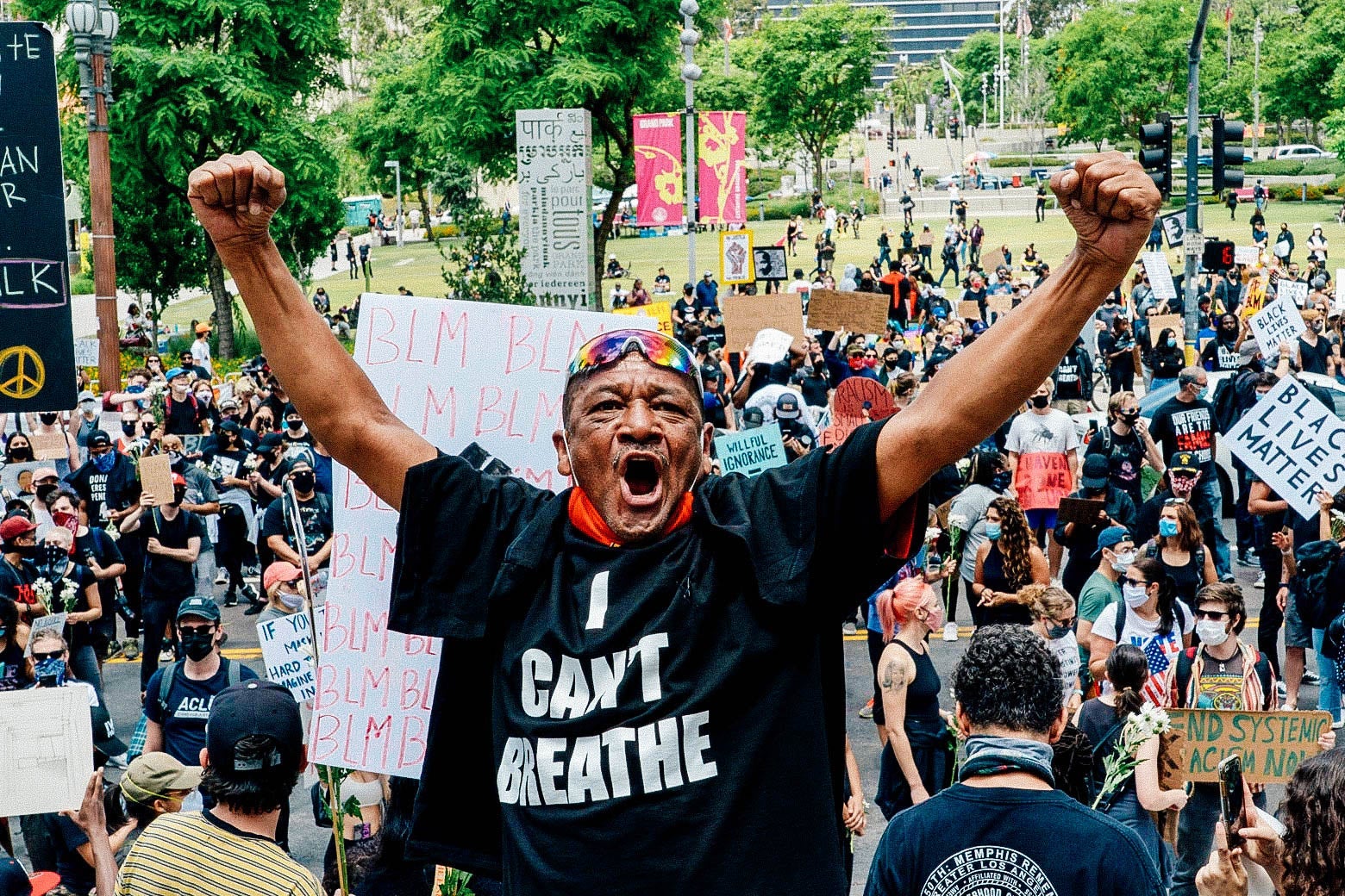 A man in a T-shirt that reads "I can't breath" holds up both arms amid a crowd of protesters.