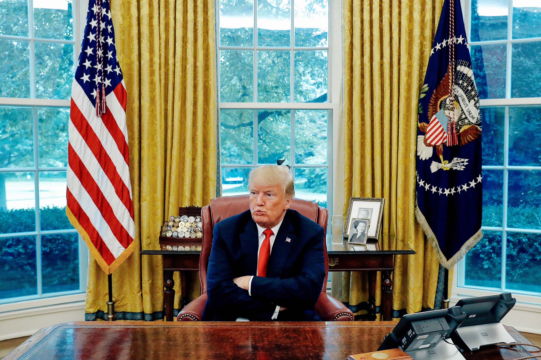 Donald Trump crosses his arms across his chest while sitting behind his desk in the Oval Office.