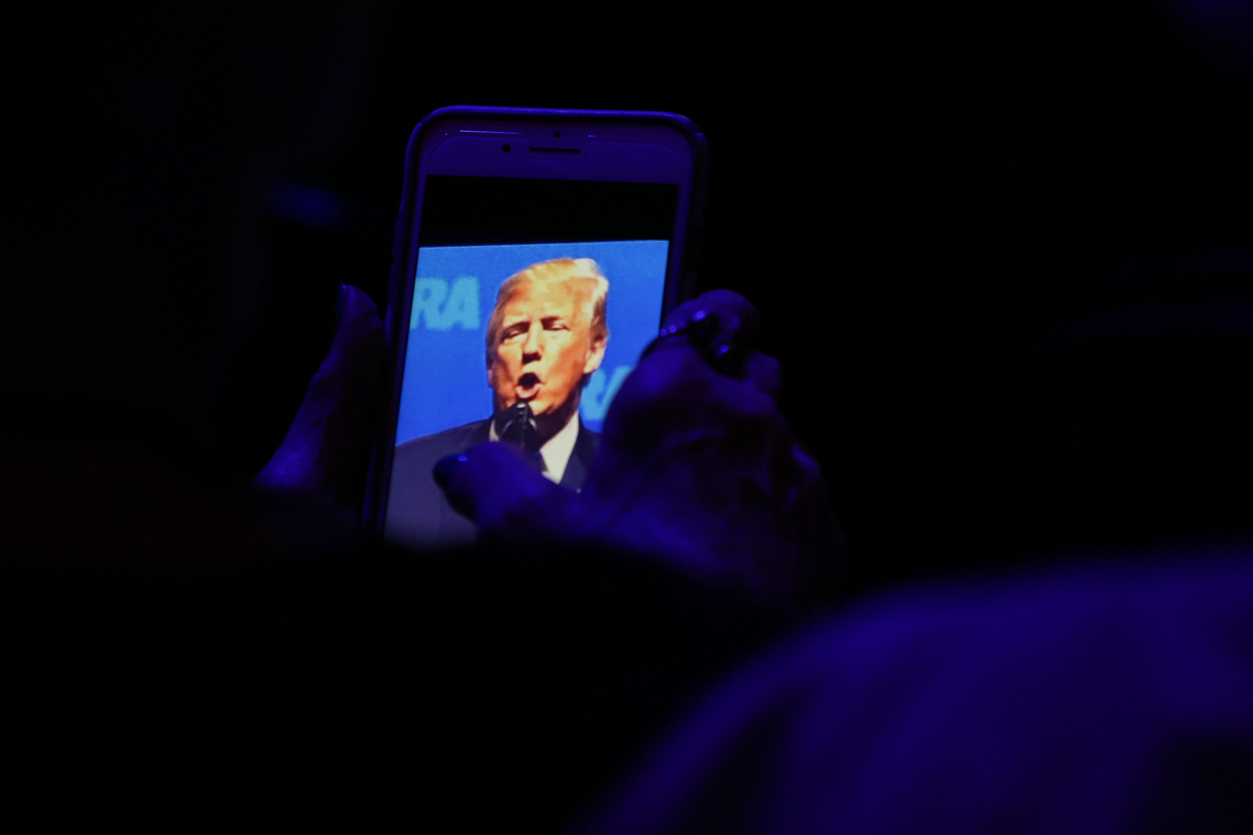 A woman snaps photos on her phone of US President Donald Trump as he speaks at the NRA-ILA Leadership Forum during the NRA Annual Meeting & Exhibits at the Kay Bailey Hutchison Convention Center on May 4, 2018 in Dallas, Texas. (Photo by Loren ELLIOTT / AFP)        (Photo credit should read LOREN ELLIOTT/AFP/Getty Images)