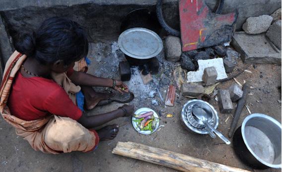 An Indian woman cuts vegetables to cook on the roadside at a temporary shelter