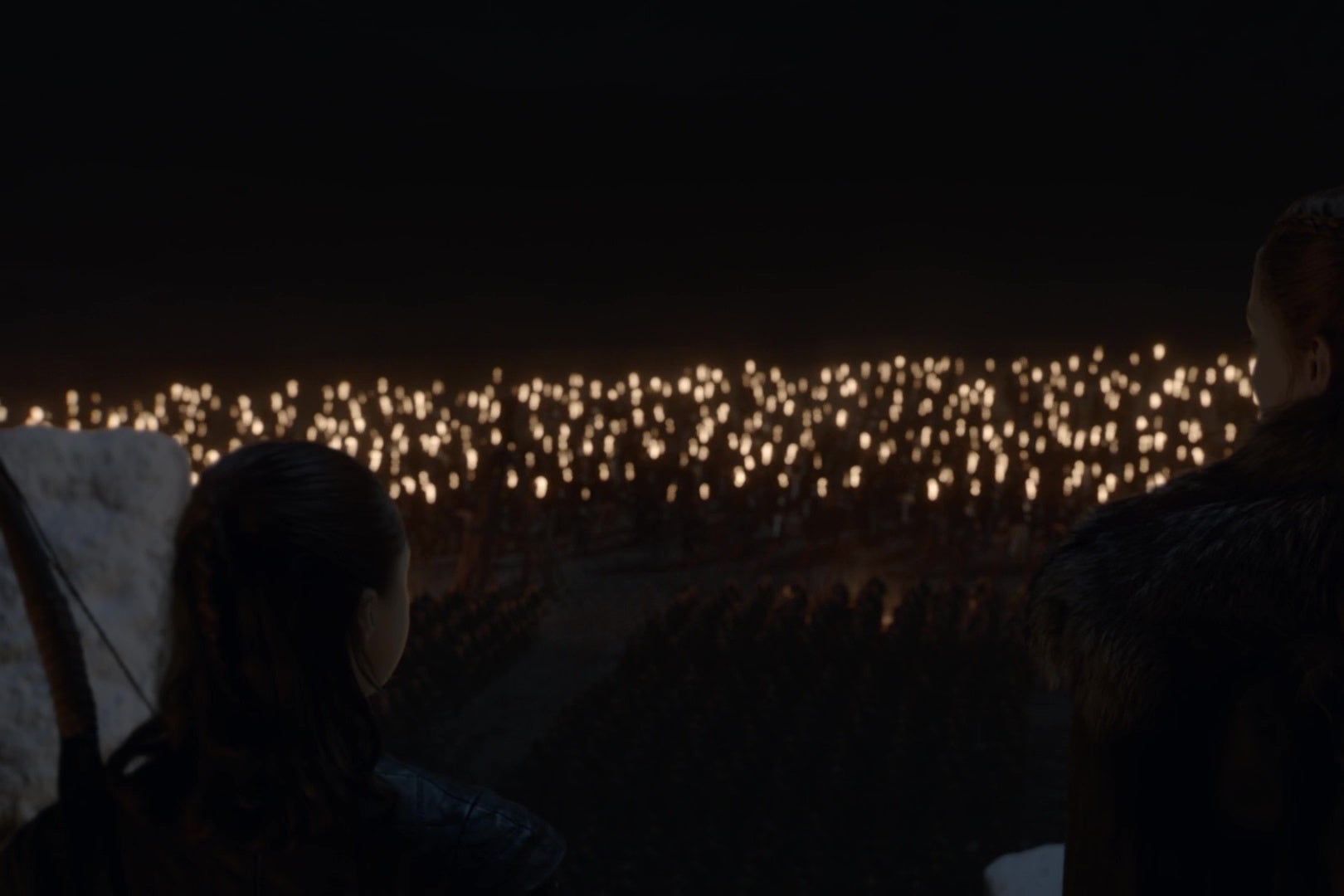 Two Game of Thrones characters watch from a castle rampart as Dothraki below begin to charge away into battle.