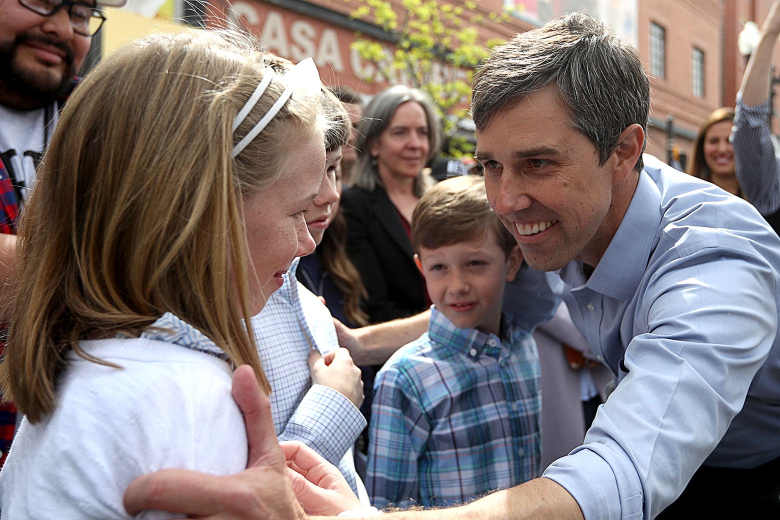 Beto O'Rourke leans down and puts his arms around his three children at an event.