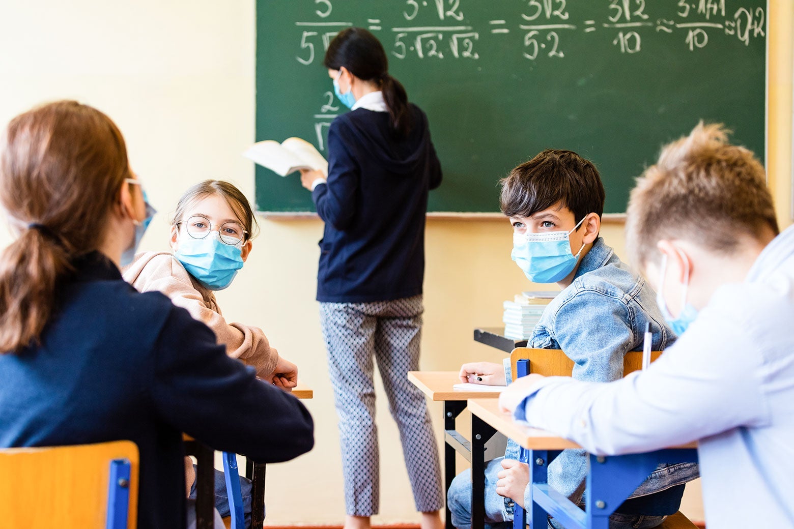A classroom with children wearing mask while seated at their desks.