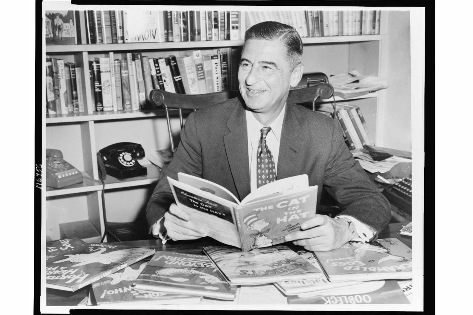 A black-and-white photo of Dr. Seuss sitting at his desk with his books