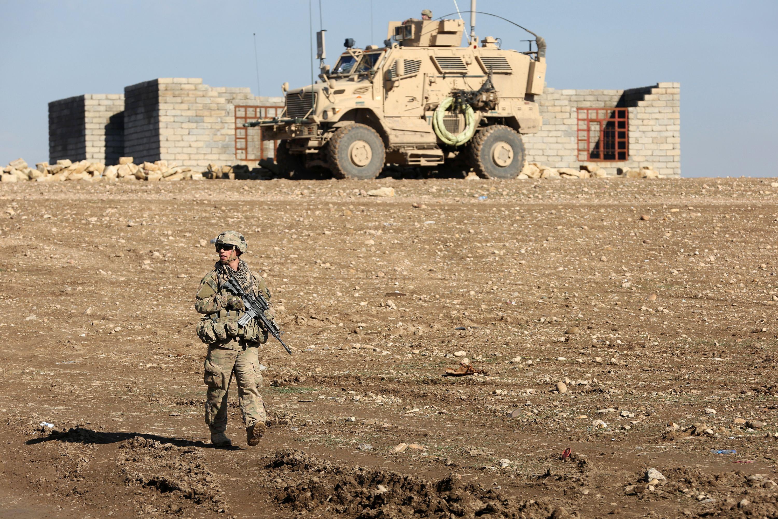 U.S. soldier on patrol with armored vehicle in stark landscape in front of small down near Mosul