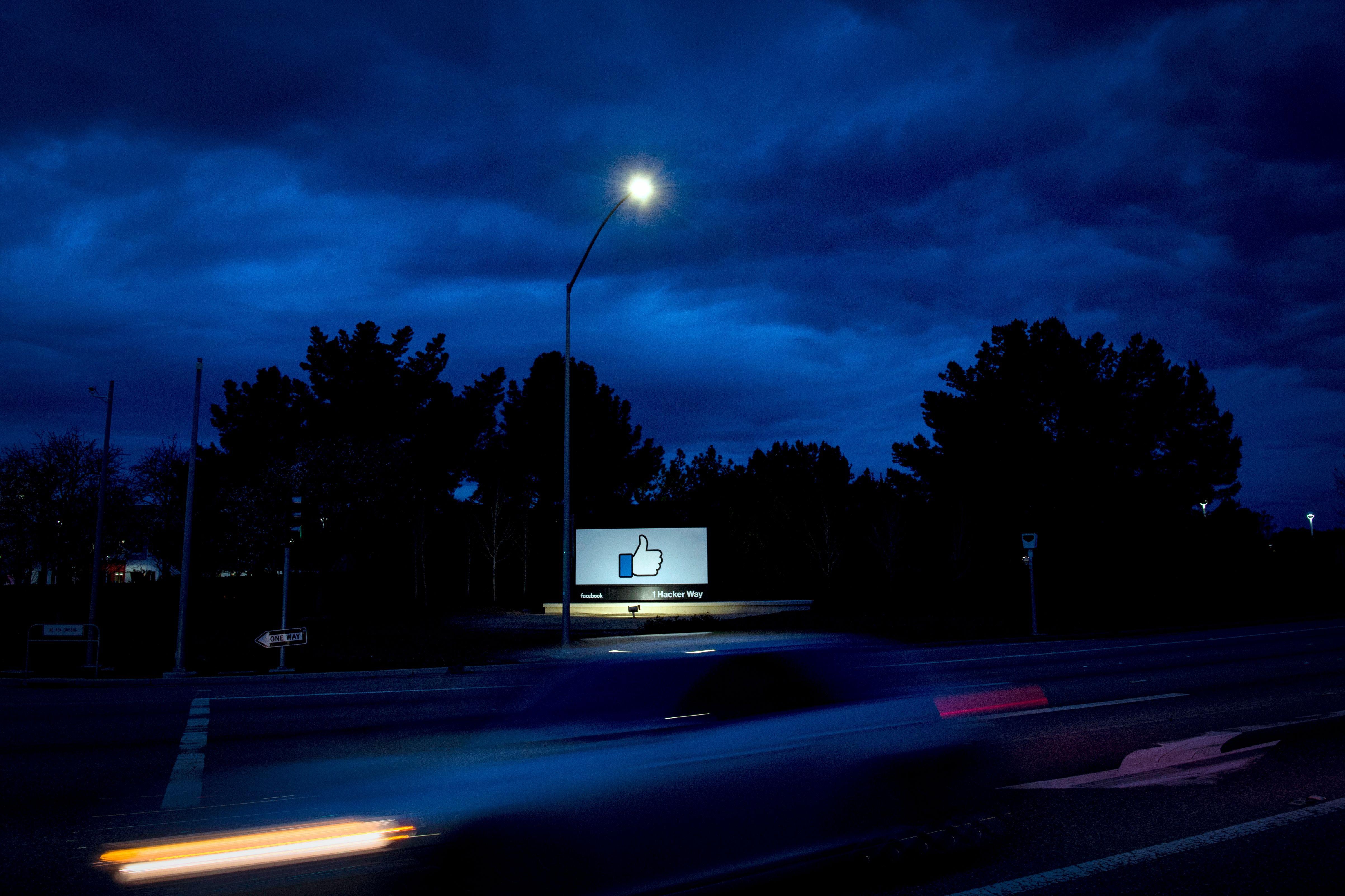 A Facebook billboard featuring the like button, by the side of a highway at night.