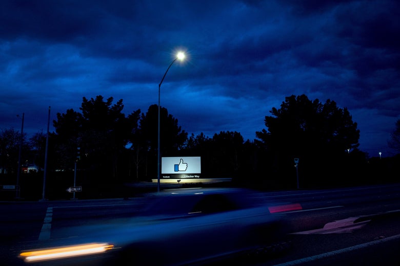 A Facebook billboard featuring the like button, by the side of a highway at night.