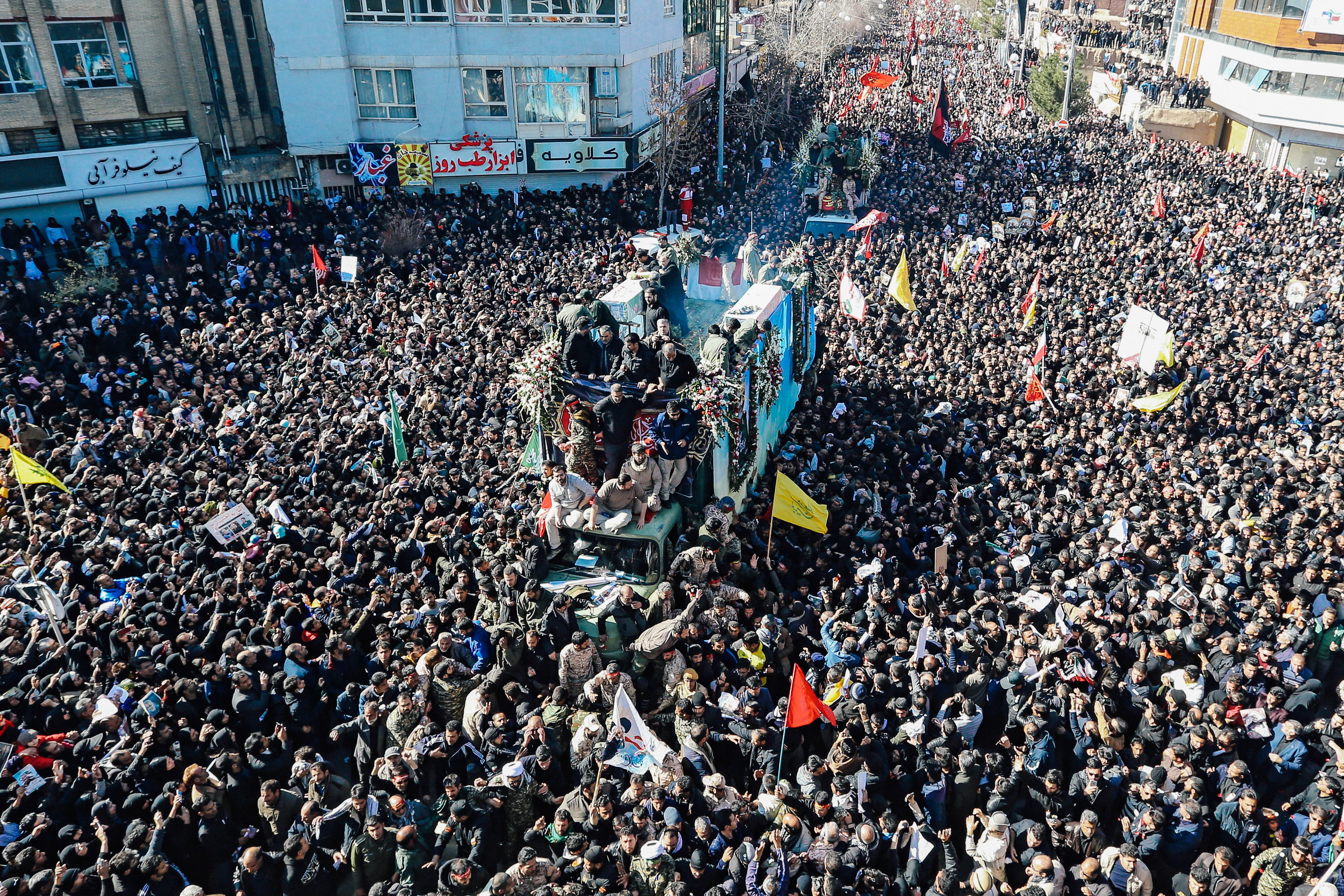 A mass of people in a city square with a vehicle in the middle.