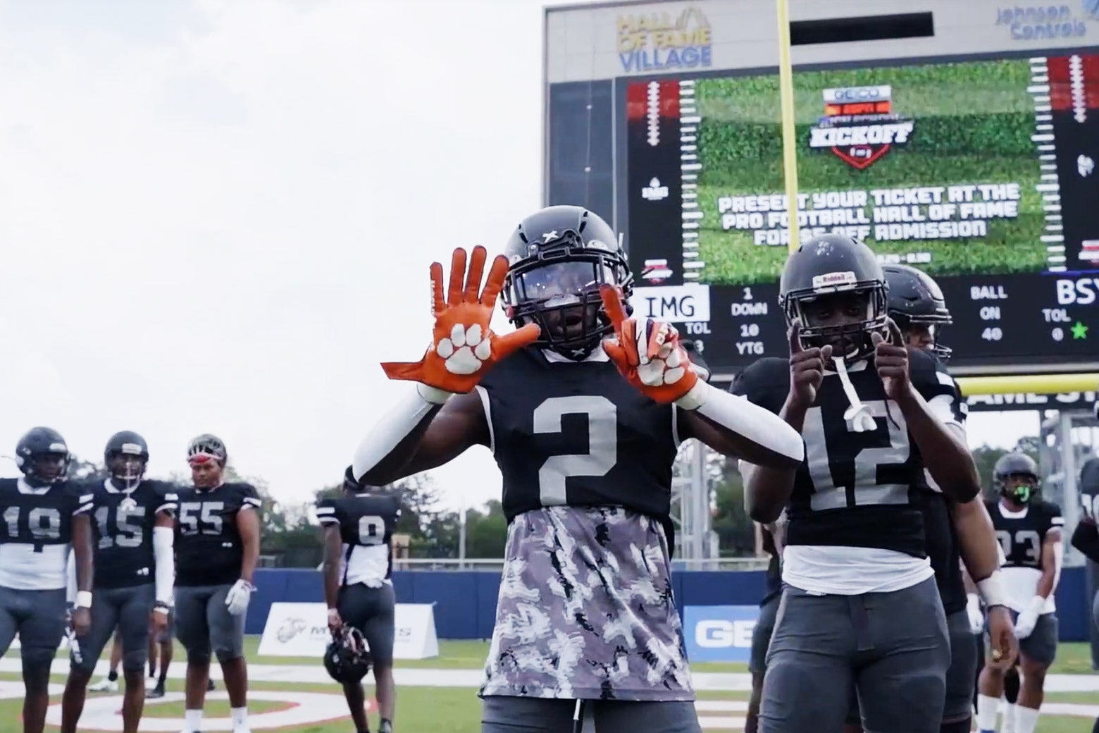 Football players from Bishop Sycamore hold up hands and point at the camera from the field