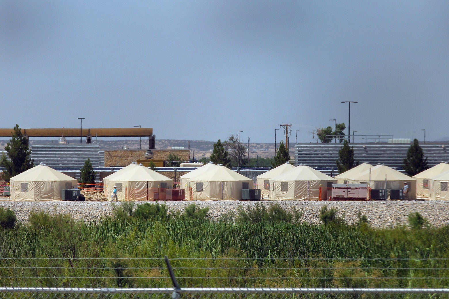 Behind barbed wire, tents are set up as a temporary detention center.