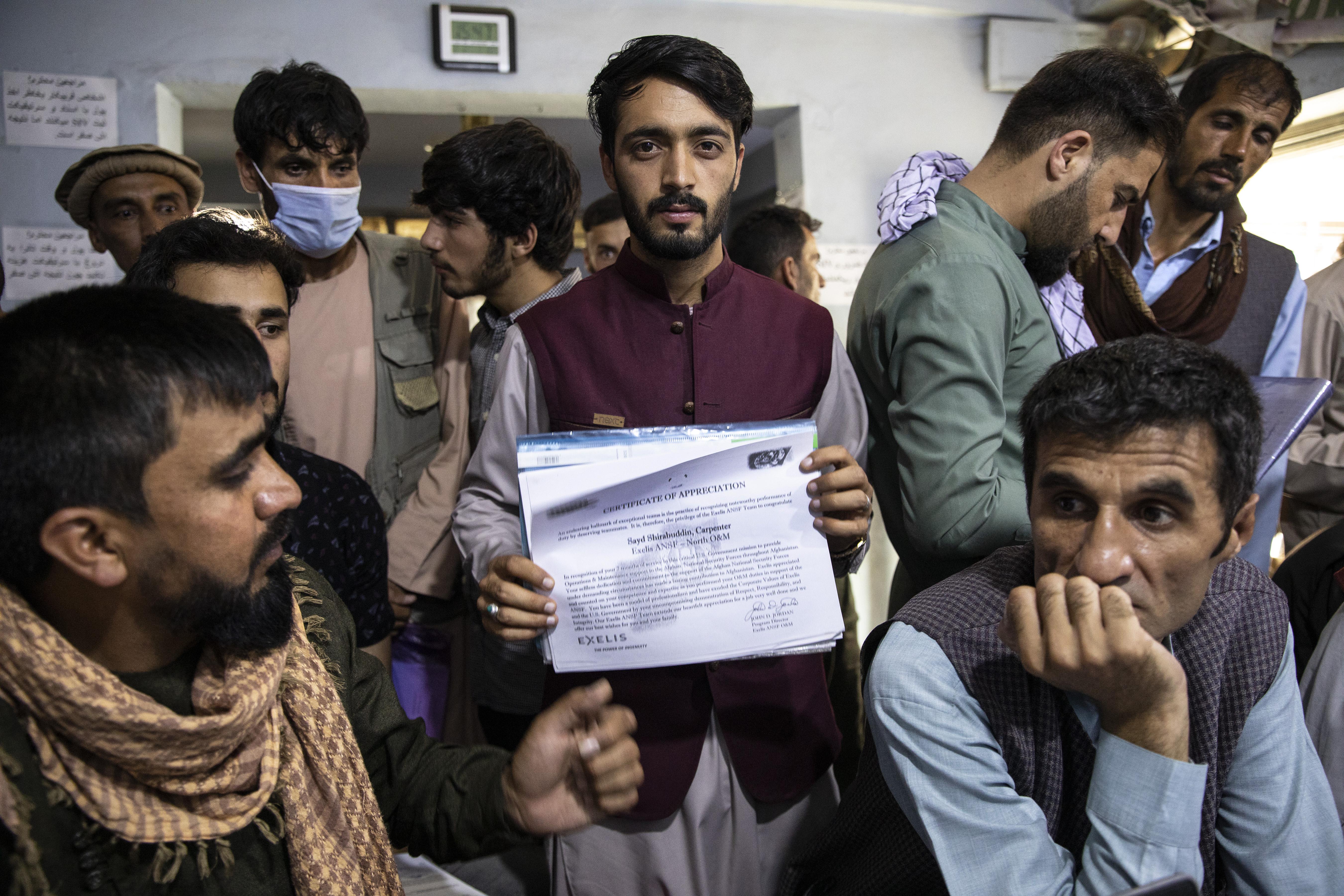 A man looks directly at the camera holding up his certificate amid a crowd of people