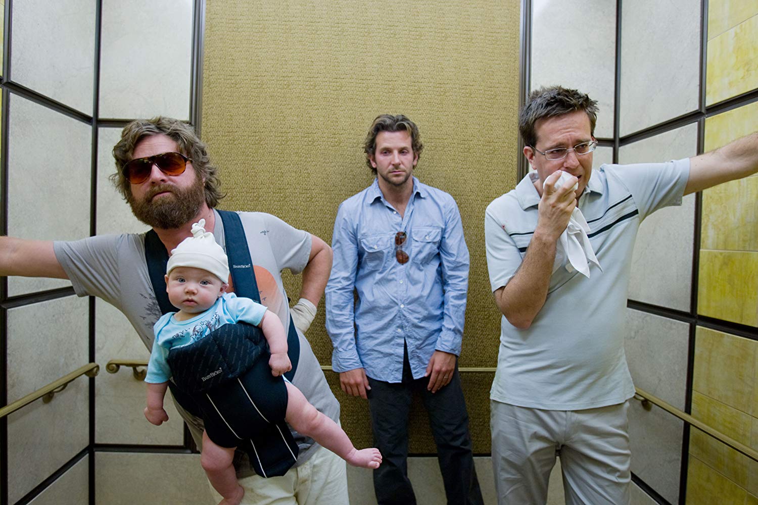 Three men in an elevator. One wears a baby in a carrier on his chest.