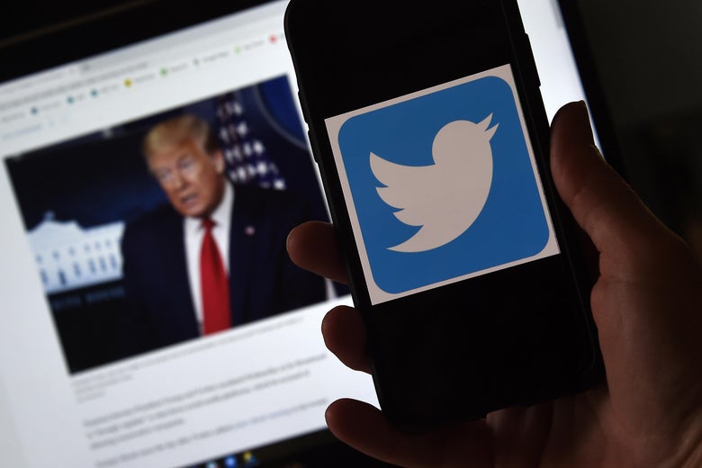 Hand holding a cellphone with the Twitter logo on-screen, in front of a laptop with a photo of Trump on-screen