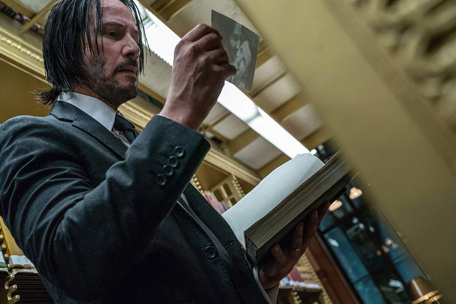 John Wick looks at a photo found inside a book, as he stands in the stacks of a library.