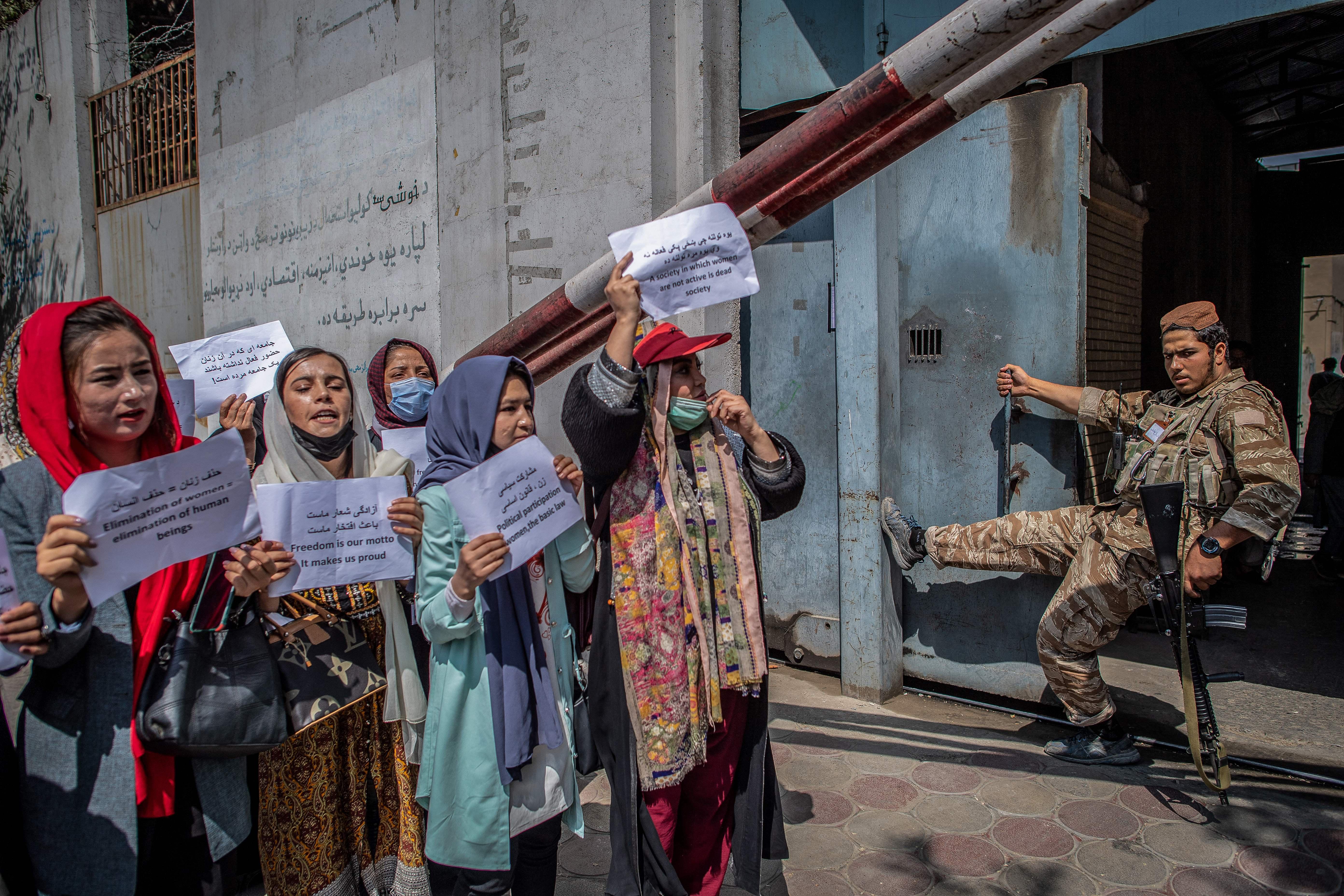 A Taliban fighter watches as Afghan women hold placards during a demonstration demanding rights for women in front of the former Ministry of Women Affairs in Kabul on September 19, 2021. 