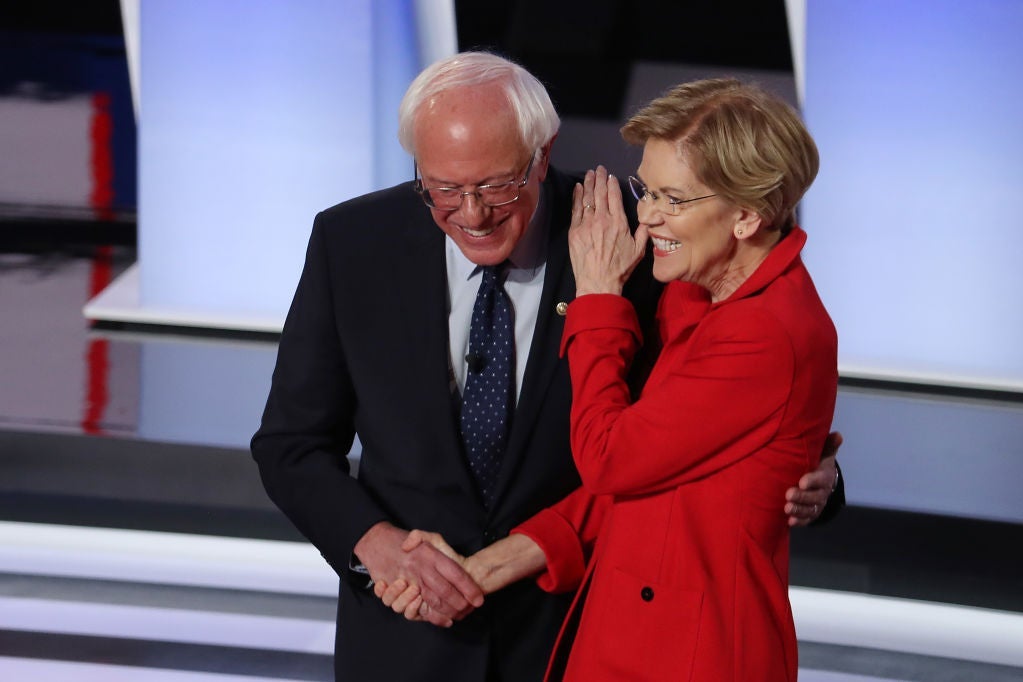 Warren and Sanders both smile as they shake hands onstage and she pats his shoulder.