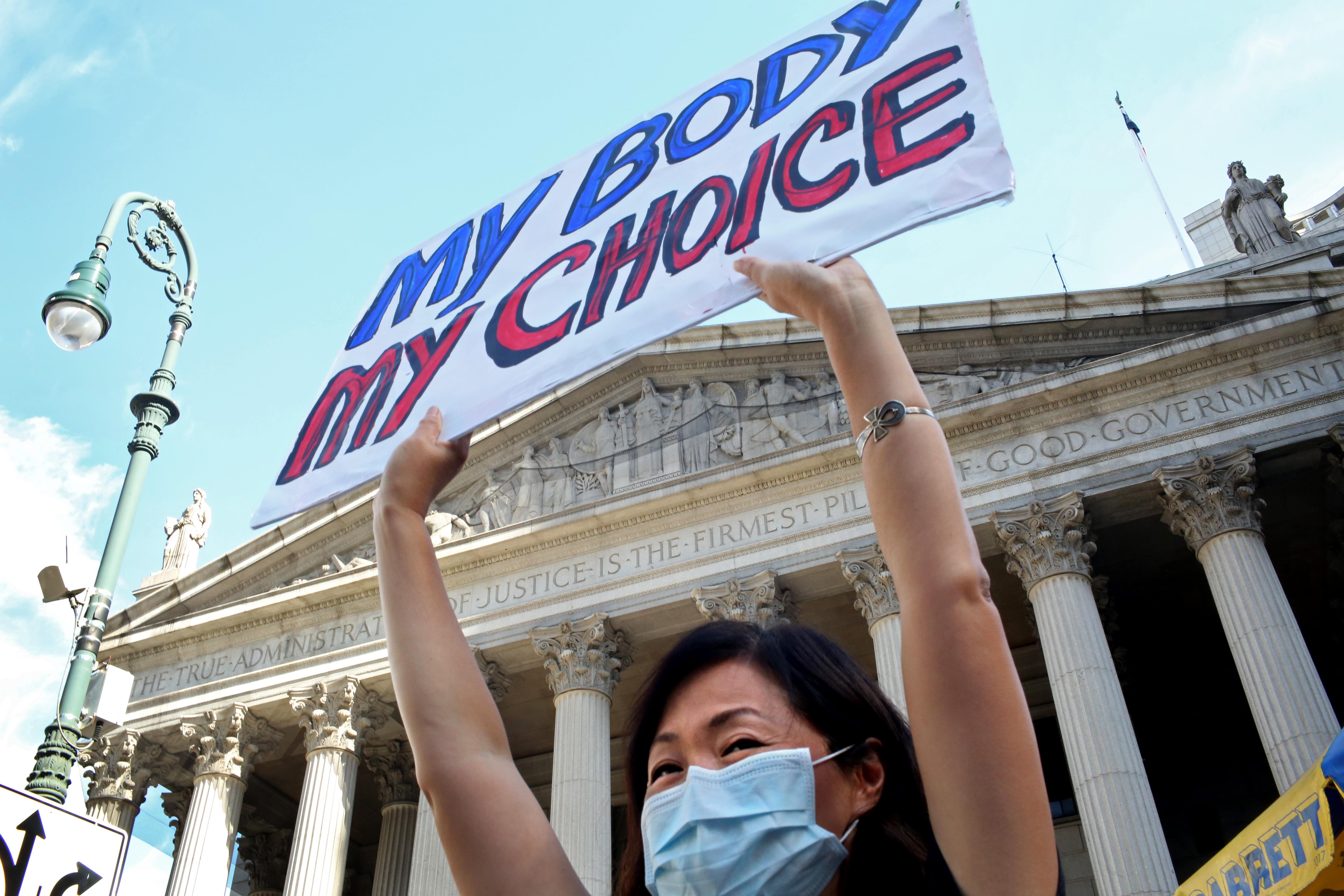 A woman in a mask holds a sign that says "my body my choice."