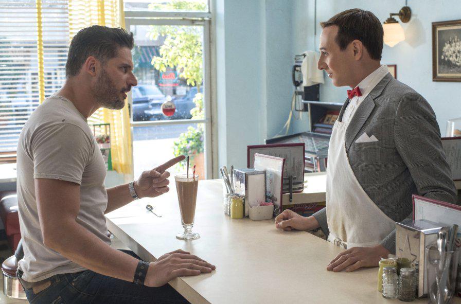 Pee-Wee stands at a 50s-style counter wearing an apron over his signature gray suit and red bowtie. Across from him, a buff and stern-looking Joe Manganiello .