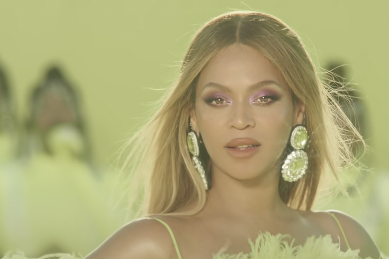 Beyonce wearing a neon yellow gown with pink eyeshadow and large yellow earrings looks at the camera