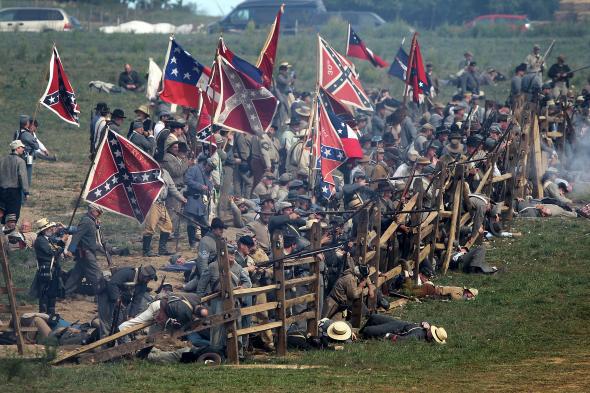 A reenacted Civil War battle, featuring soldiers with rifles and horses waving Confederate flags.