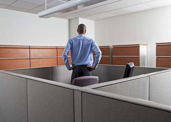 Businessman standing at his desk, trapped in cubicle, rear view