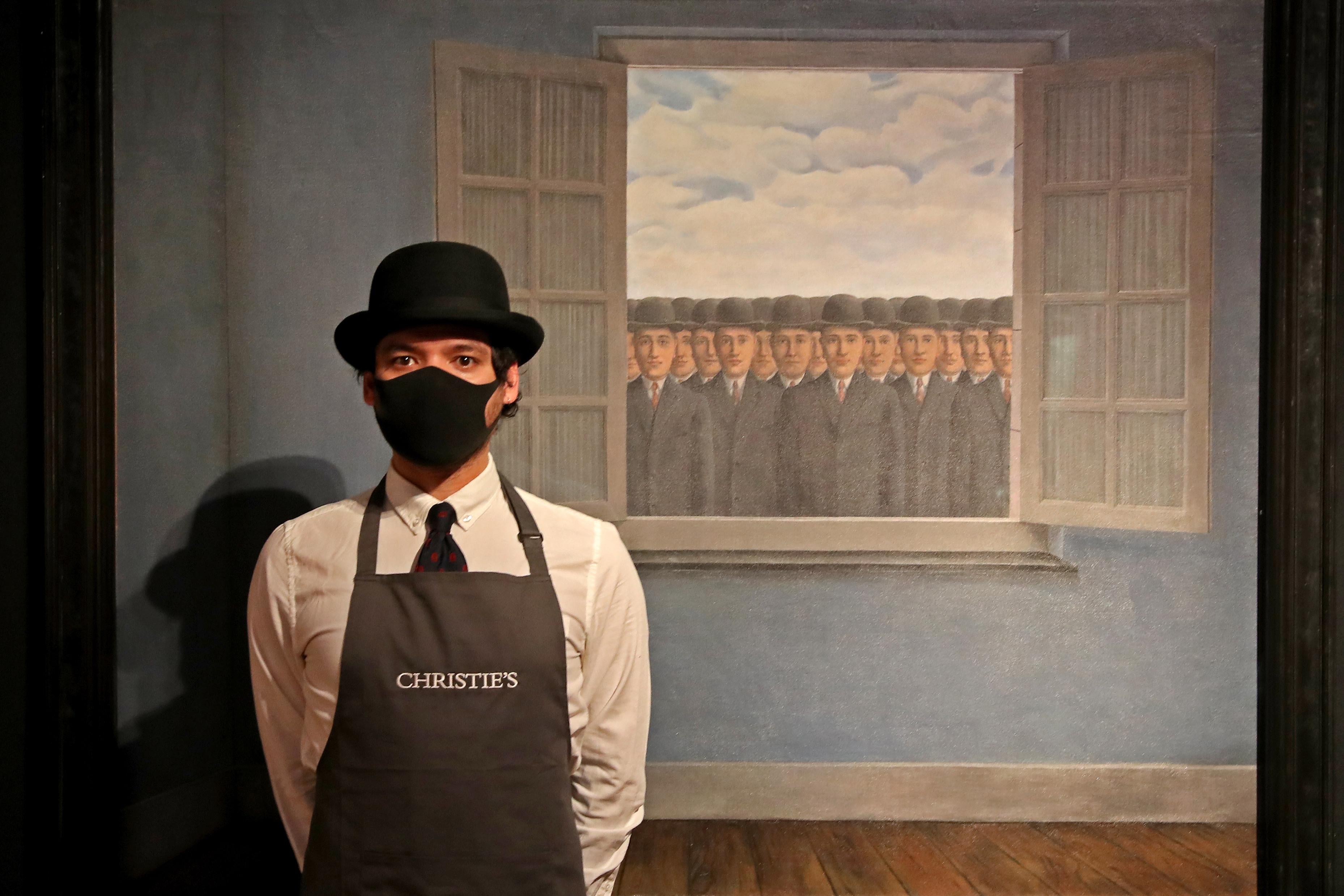An art worker wearing a bowler hat and a Christie's apron stands next to René Magritte's "Le mois des vendanges" painting, which features an infinite number of men wearing bowler hats peering in an open window.