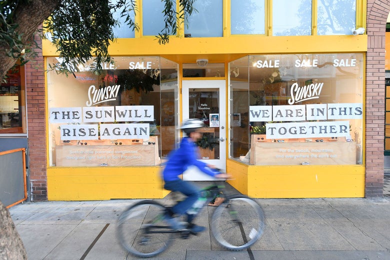 Someone bikes by a Sunski storefront that reads "We are in this together" and "The sun will rise again."