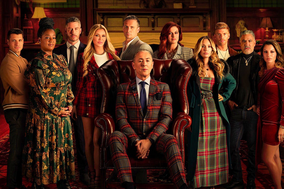 Alan Cumming, the host of the reality TV show 'The Traitors,' wears a tartan suit and is seated, with the cast surrounding him.