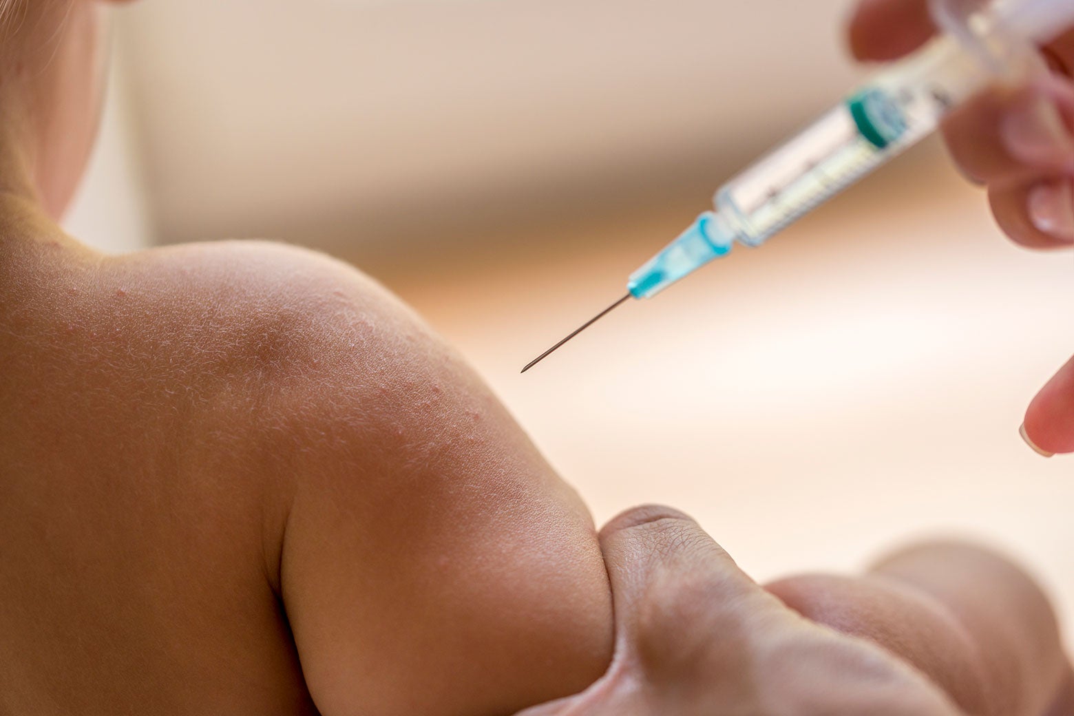 A syringe approaching a child's arm, which is being squeezed to prepare for the injection.