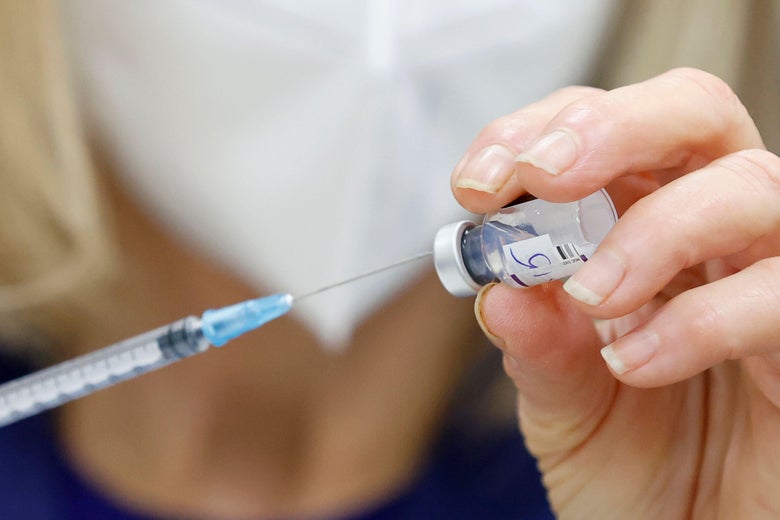 A syringe going into a vial of vaccine held in a person's hand