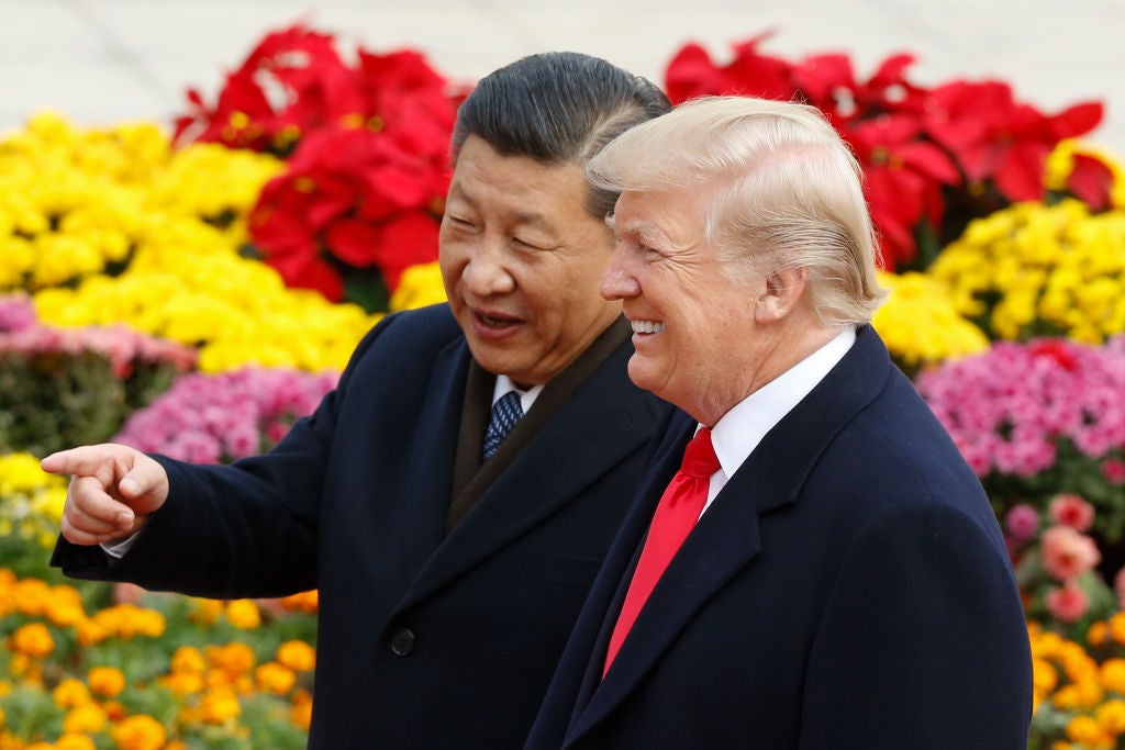Xi and Trump stand in front of colorful flowers as Xi points and Trump smiles.
