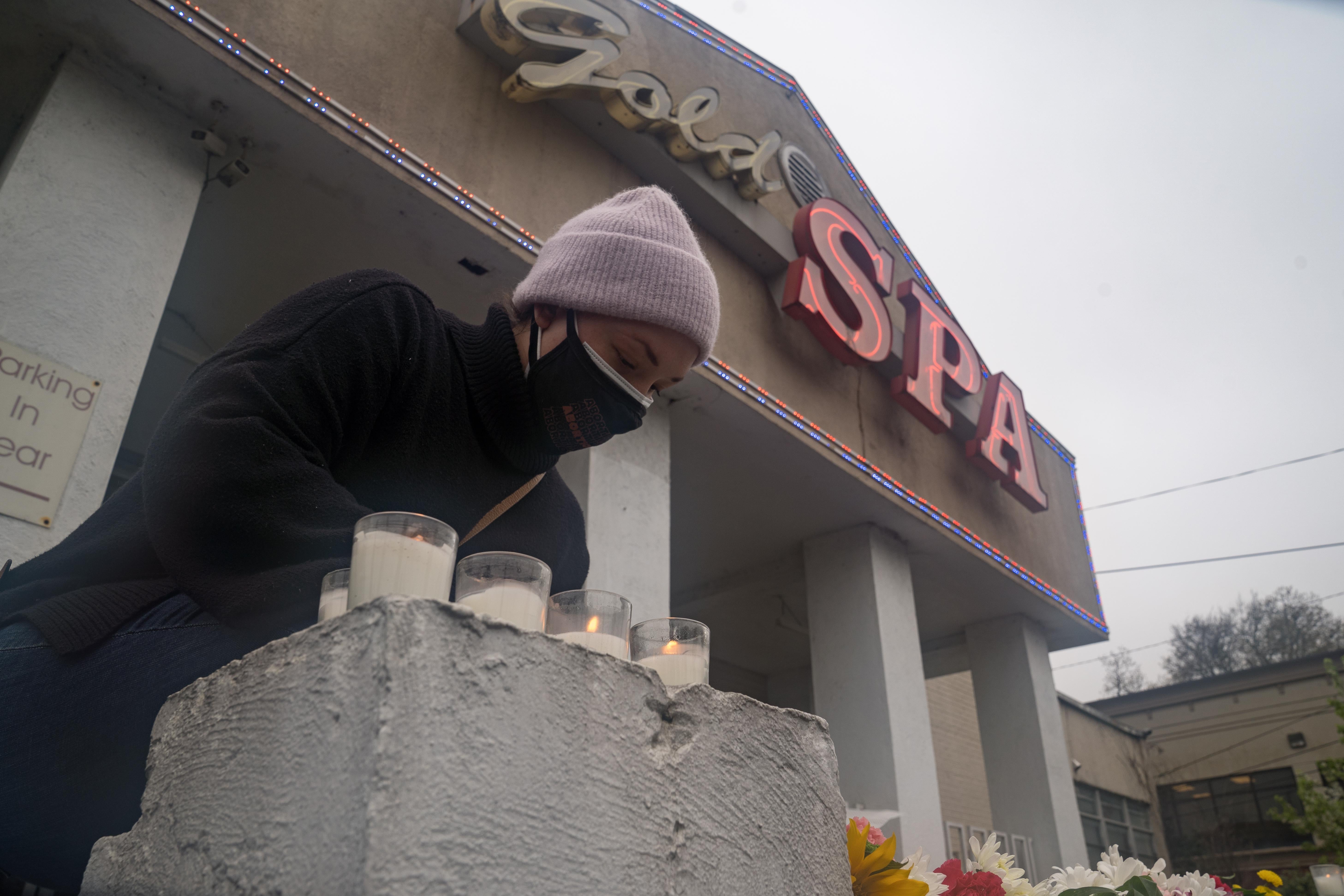 Mourner Erica Gonzalez leaves flowers at a memorial with candles outside Gold Spa.