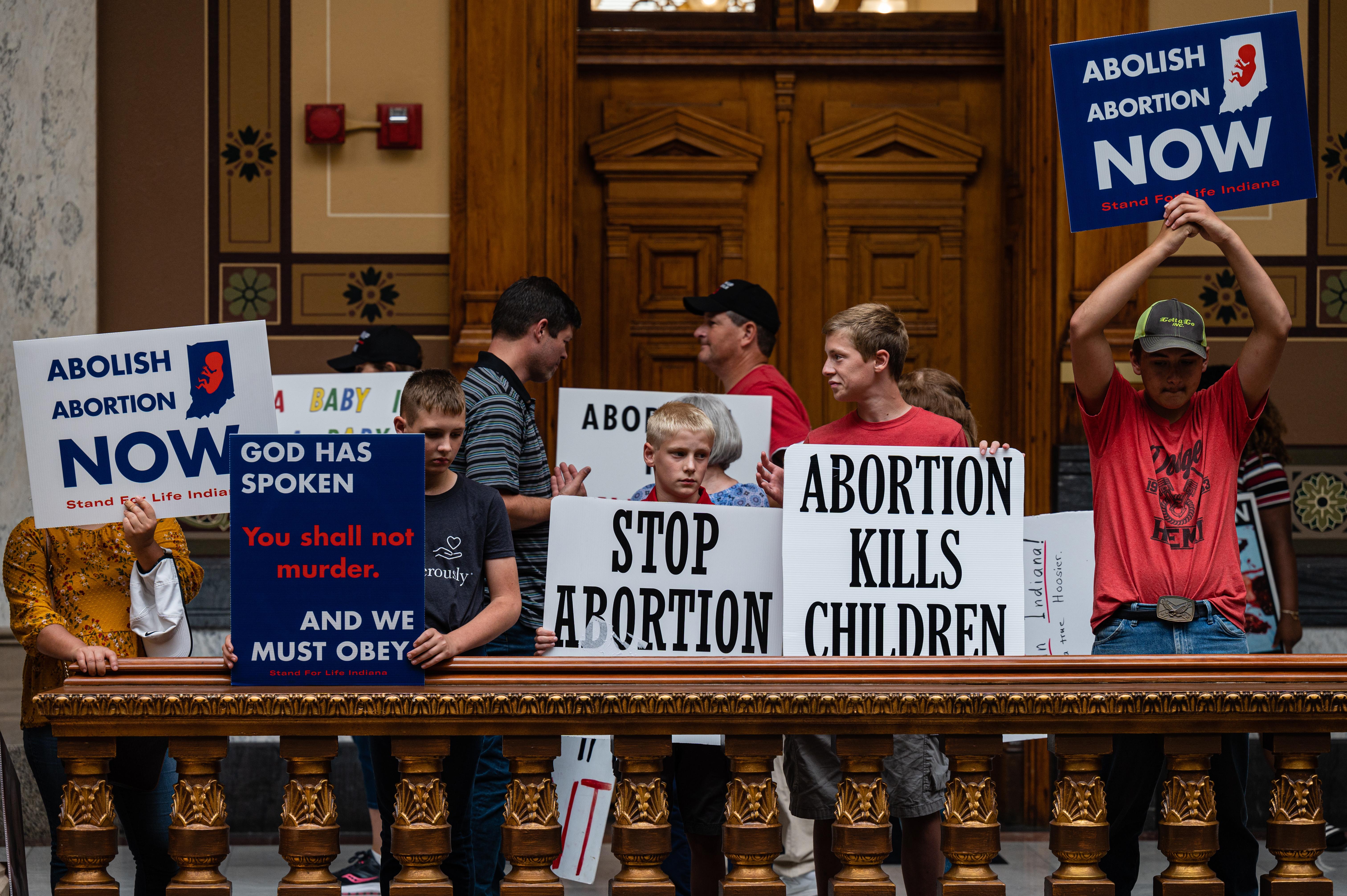 Anti-abortion protesters hold up signs inside of the Indiana State Capitol building on July 25, 2022 in Indianapolis, Indiana. Signs say "STOP ABORTION" and "Abortion Kills Children."