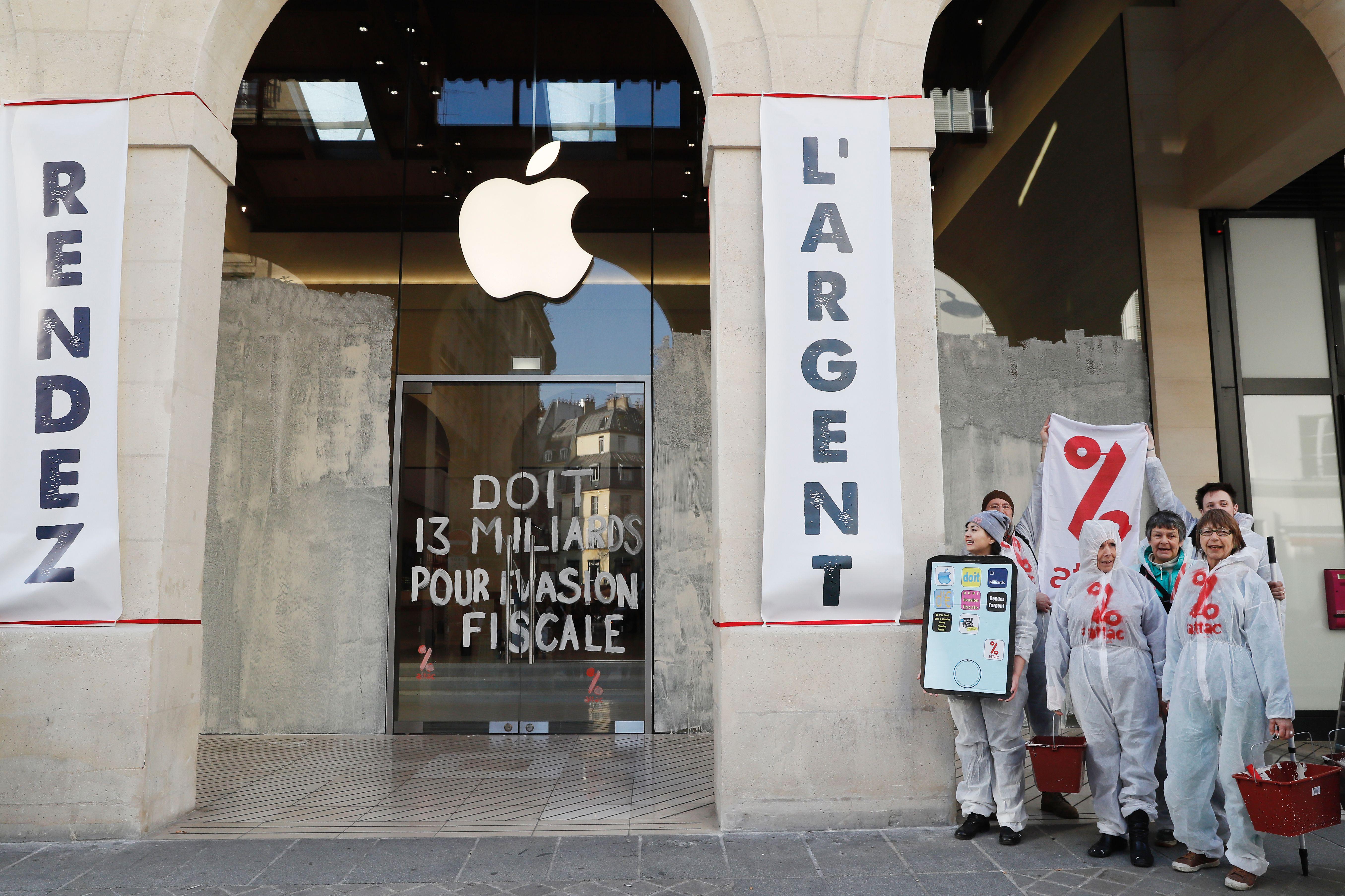 Activists from the Association for the Taxation of financial Transactions and Citizen's Action (ATTAC) pose with placards and an inscription which translate as 'Give the money back' and  '(Apple) owes 13 billion (euros) due to tax evasion' in front of an Apple store in Paris during a demonstration to denounce tax avoidance on March 13, 2017.    