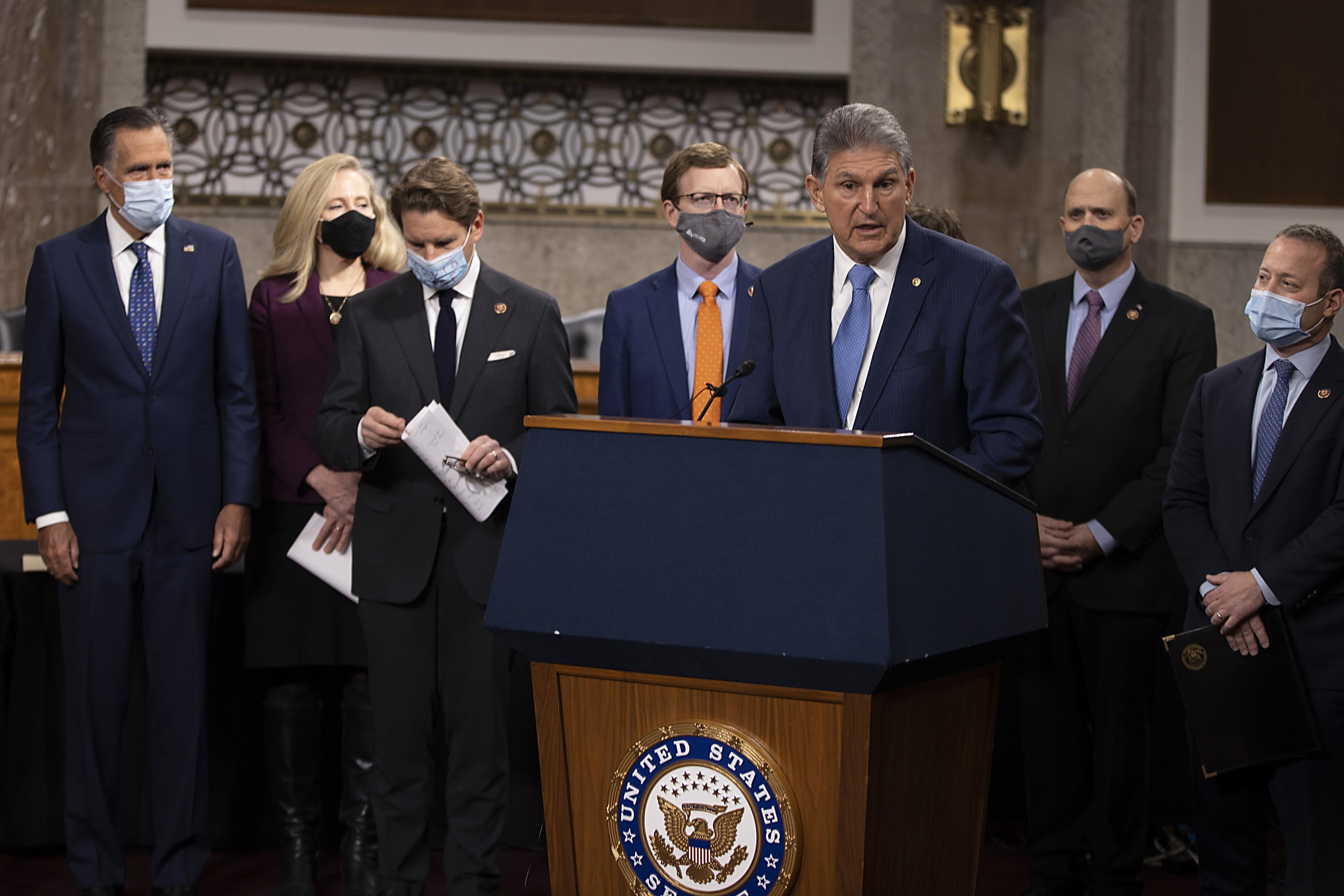 Joe Manchin speaks at a podium, surrounded by colleagues in masks.