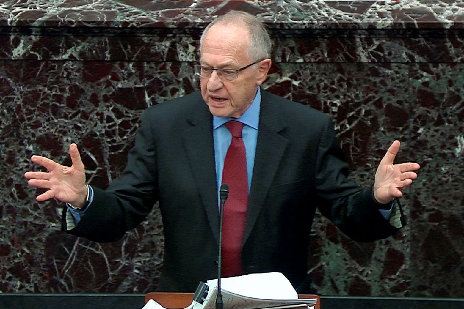 Dershowitz raises his arms while speaking at a mic before the Senate.