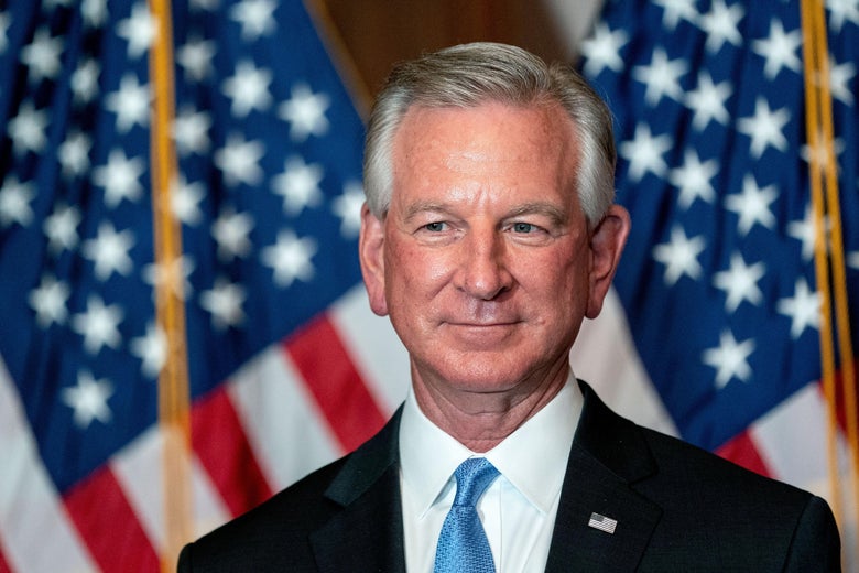 Tommy Tuberville smiling, with American flags in the background