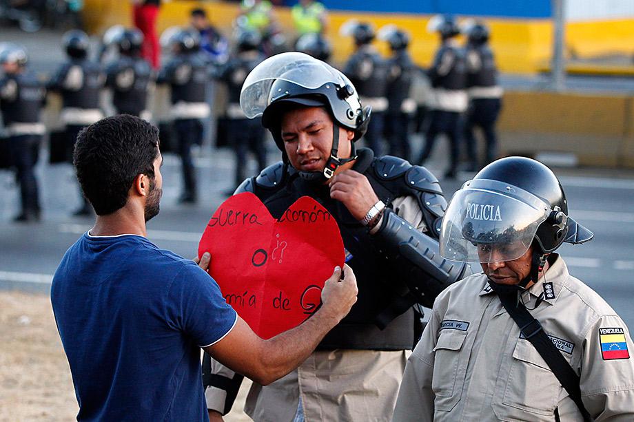 An opposition demonstrator gives a heart-shaped cutting to a police officer as demonstrators block the city's main highway during a protest against Nicolas Maduro's government in Caracas.