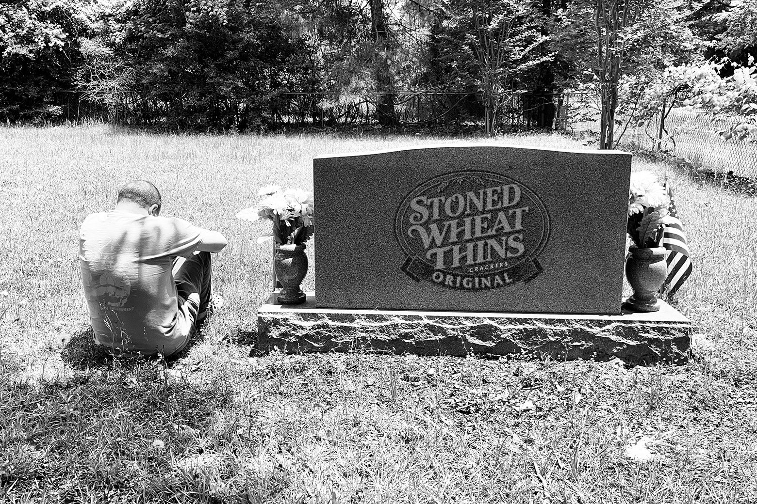 A man grieving on the ground at a cemetery next to a Stoned Wheat Thins tombstone.