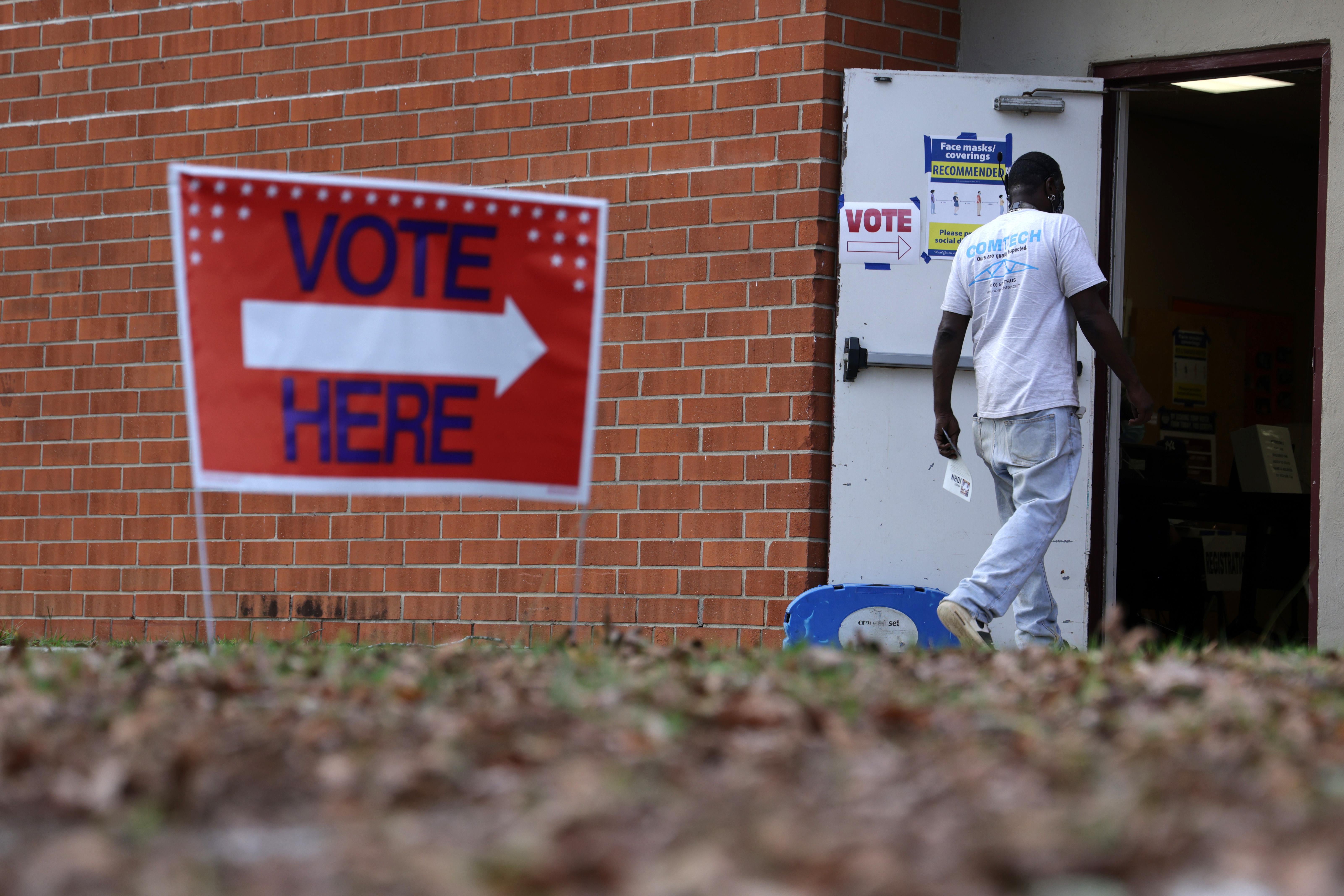 A man walks through the open door of a brick building that has a "Vote Here" sign out front