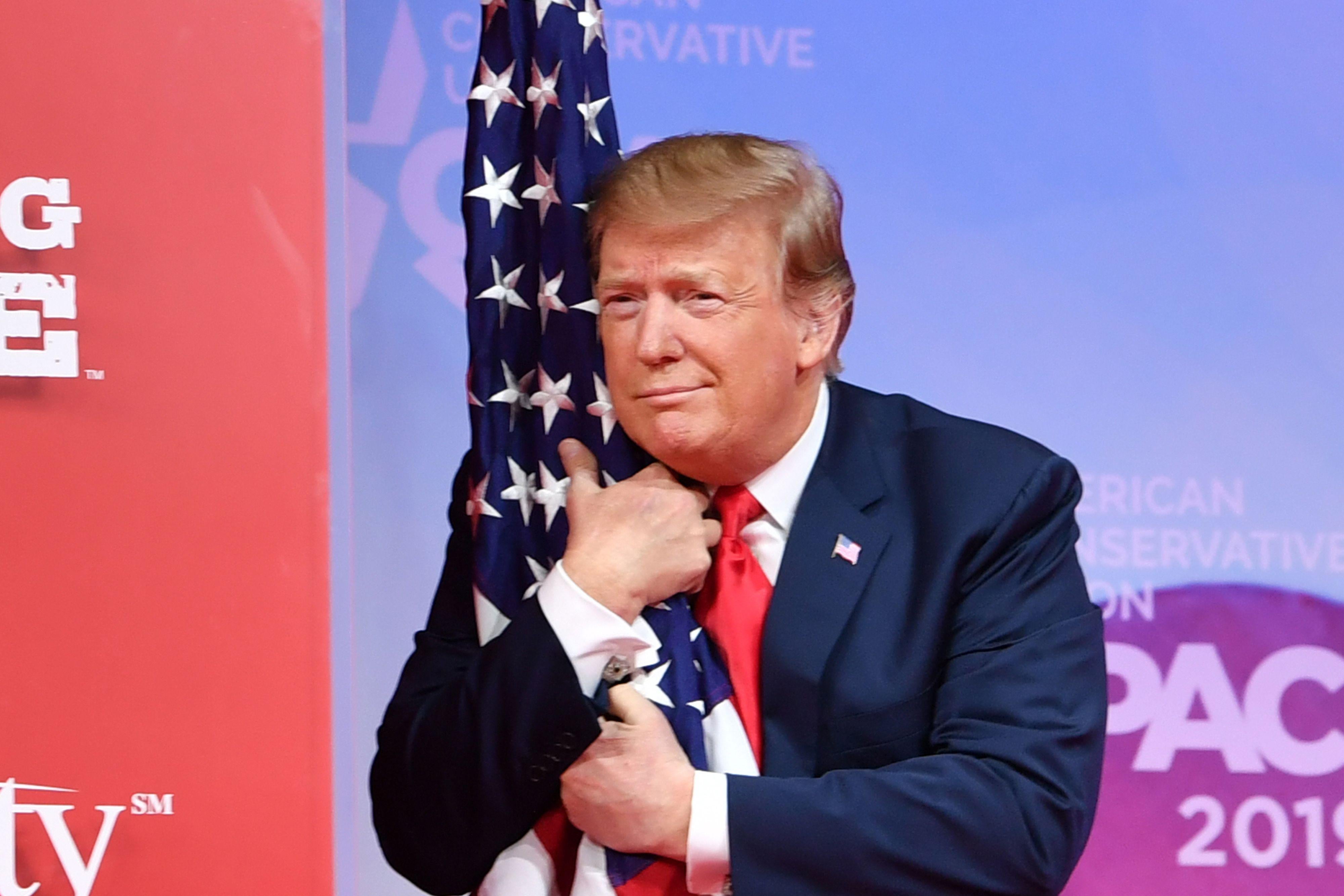 President Donald Trump hugs the flag as he arrives to speak at the annual Conservative Political Action Conference (CPAC) in National Harbor, Maryland, on March 2, 2019. 