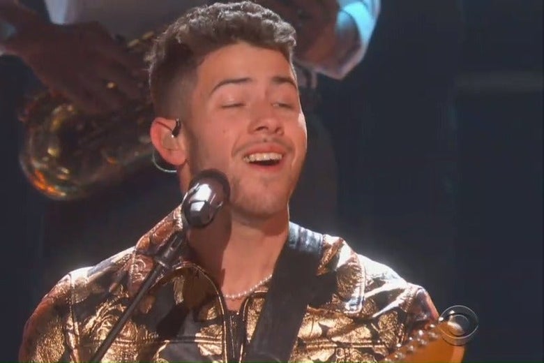 Nick Jonas sings into a microphone at the Grammys, and a piece of food can be seen stuck in his teeth.