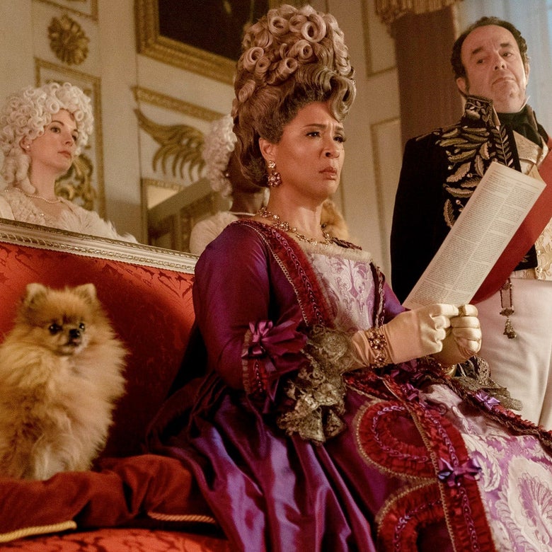 Golda Rosheuvel as Queen Charlotte in Bridgerton, sitting on a couch and positioned between a dog and a standing man
