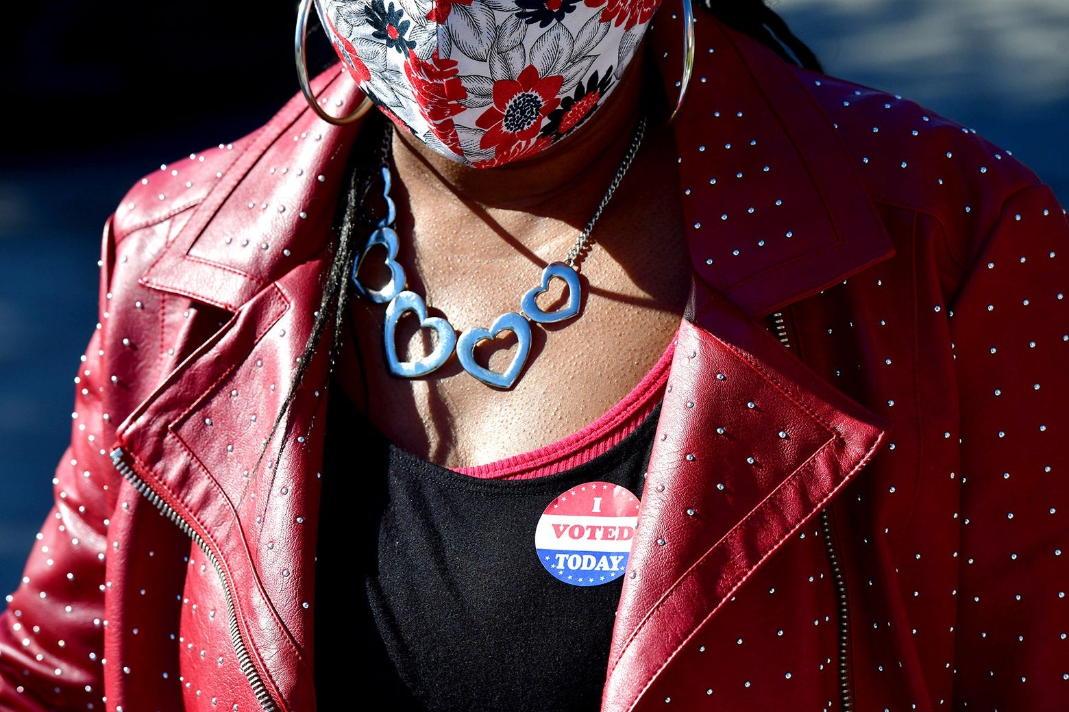 A Black woman in a red leather jacket with an I voted sticker and a mask on.