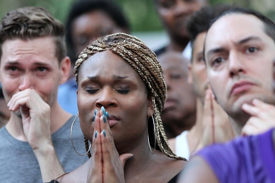 A woman in a crowd holds her hands up to her face as if in prayer.
